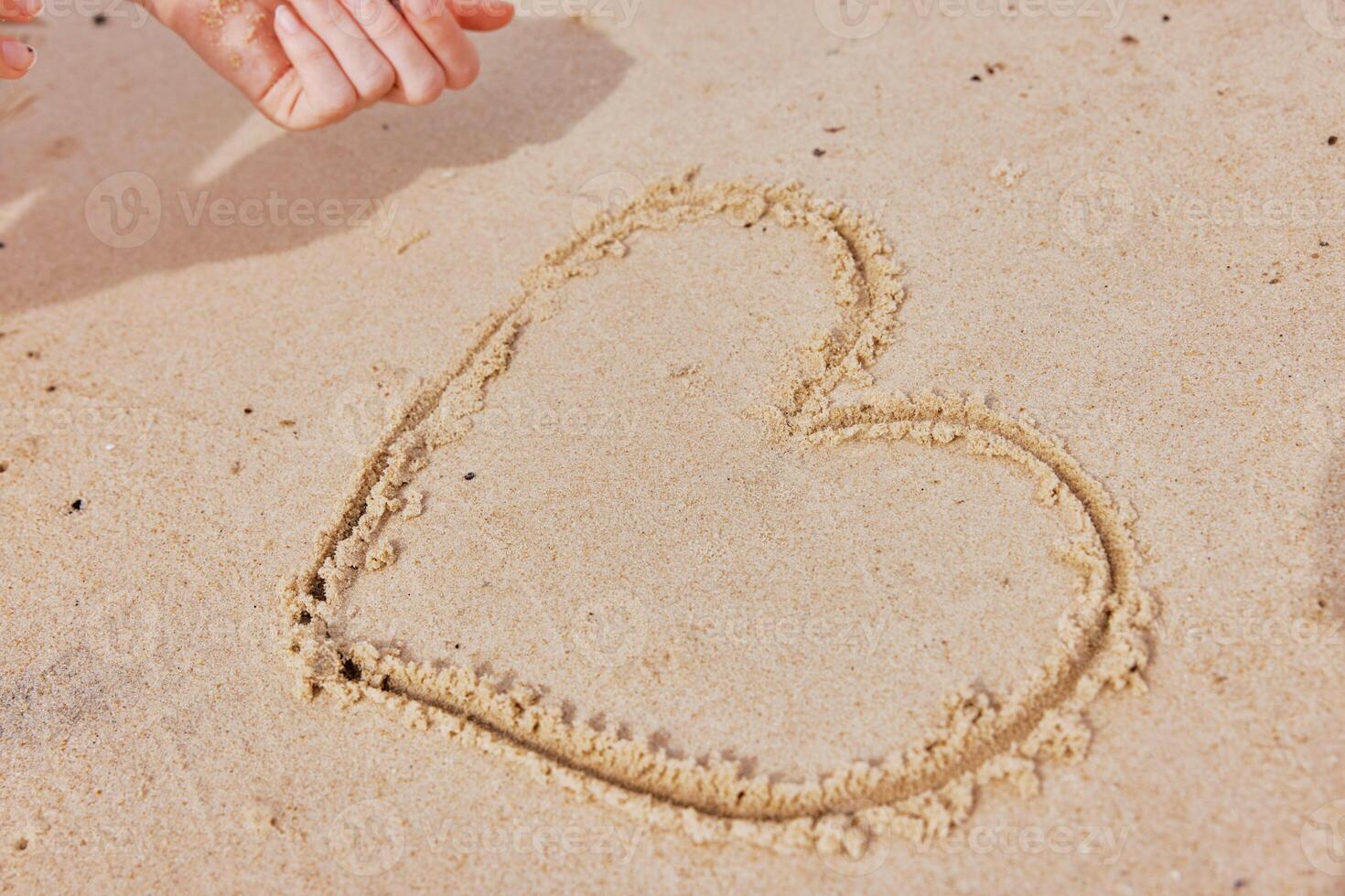 Child drawing heart shape in sand on beach. hand of kid creating symbol of love in the sand near the photo