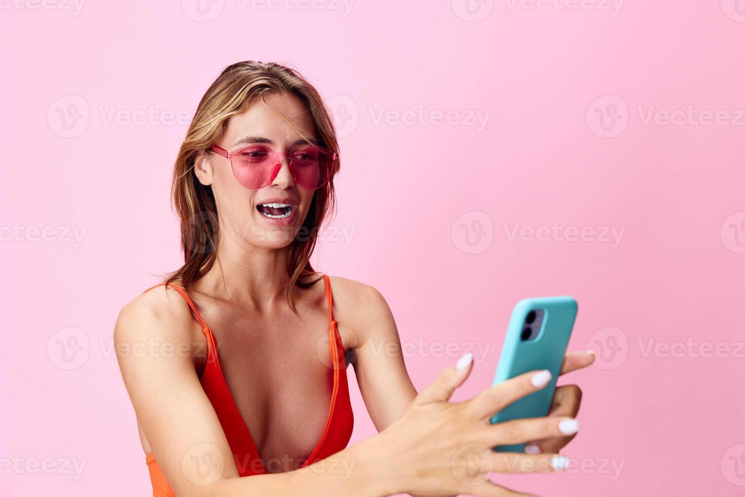 Beautiful young woman in a stylish swimsuit smiling while taking a selfie with her cell phone on photo
