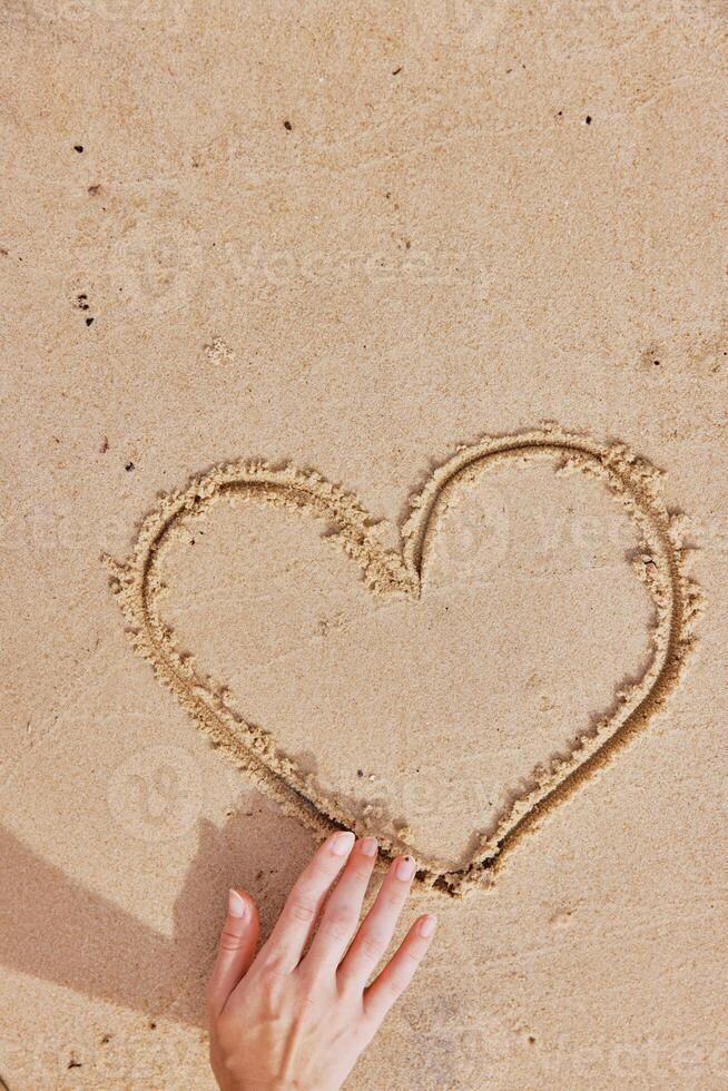 Man drawing heart on sandy beach with one hand, while making a heart shape with the other hand. photo