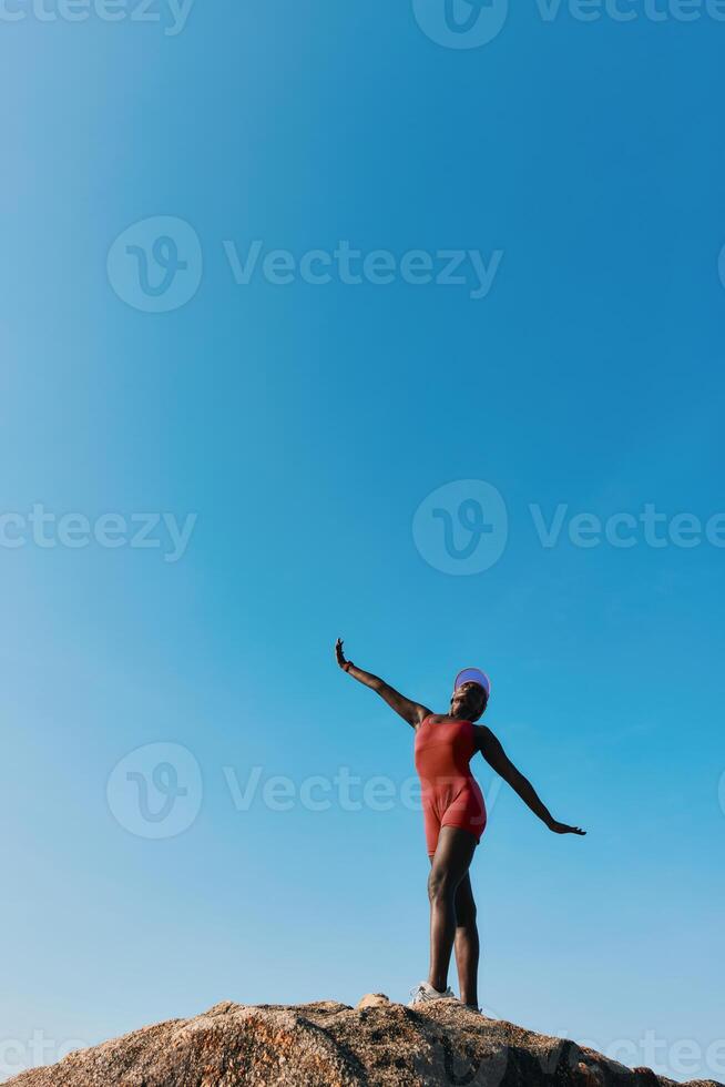 A swimmer in a red swimsuit poses gracefully on a rock, with a bright blue sky in the background photo