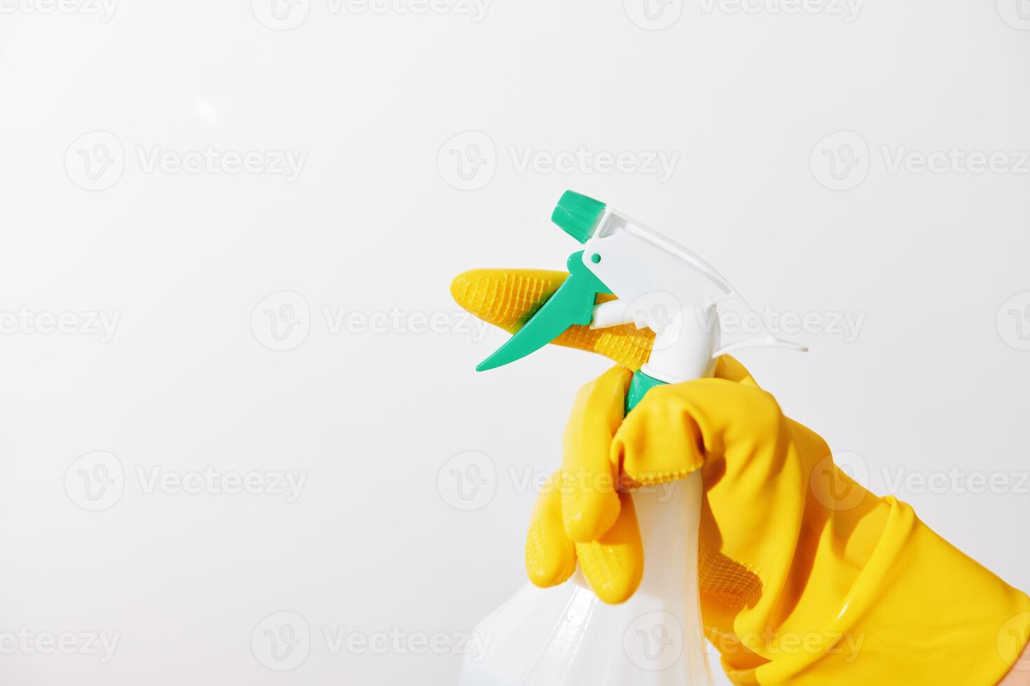 Woman in yellow rubber gloves holding a green spray bottle on white background with copy space photo