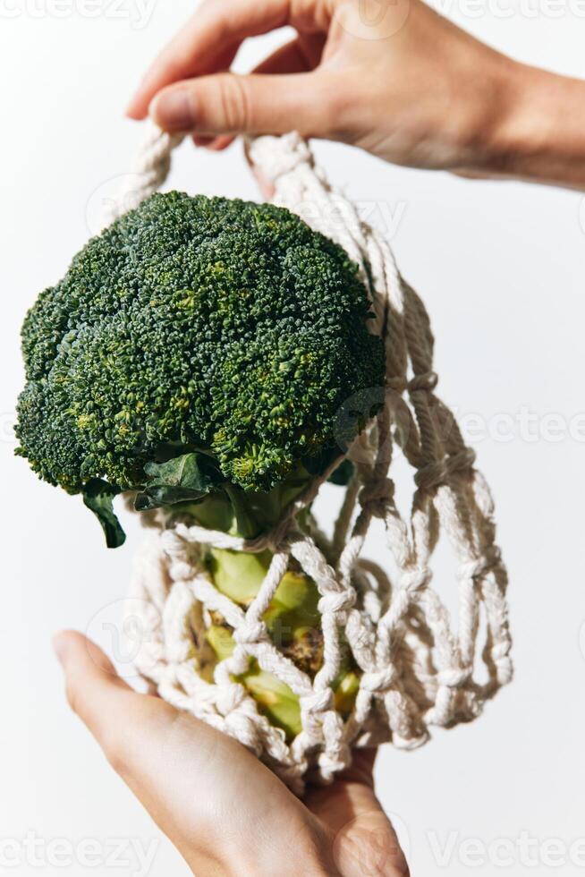 Green broccoli in net bag held by person on white background. photo