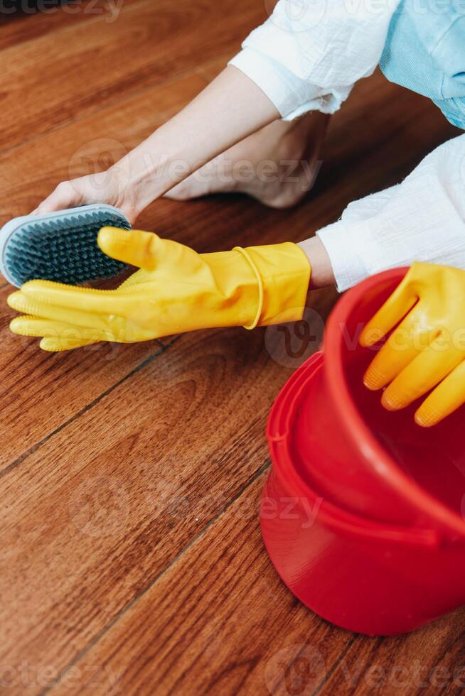 Woman cleaning wooden floor with mop and bucket of water wearing rubber gloves. photo