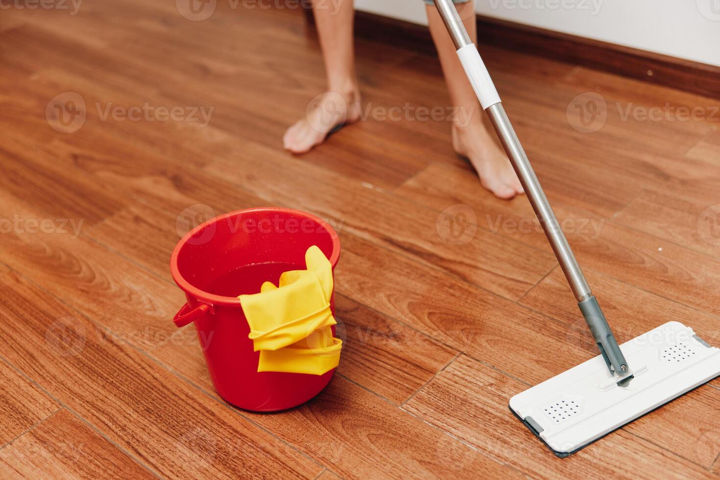 Woman mopping wooden floor with cleaning solution and bucket. red bucket and yellow rag nearby. photo