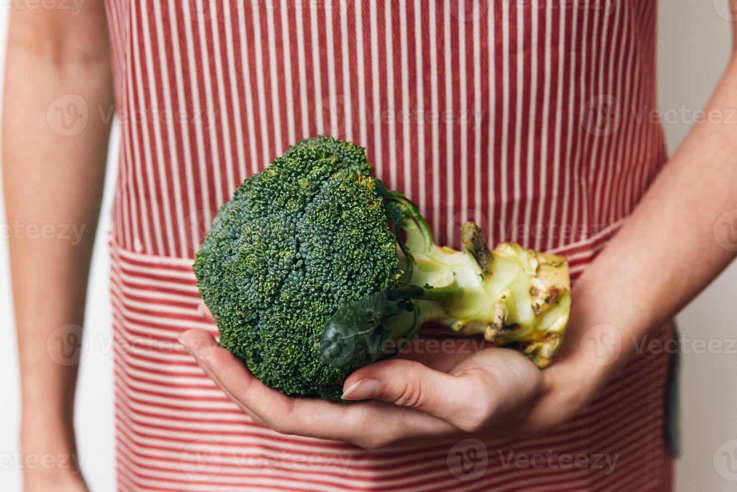 Person holding broccoli in front of red and white striped background. close-up shot focusing on the photo