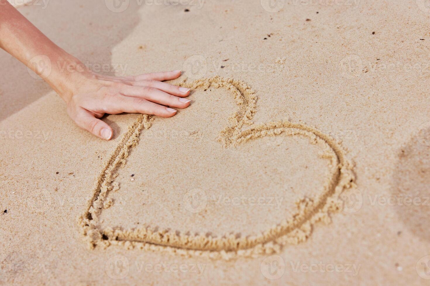 Hand drawing heart in the sand on a sandy beach with the ocean in the background. photo