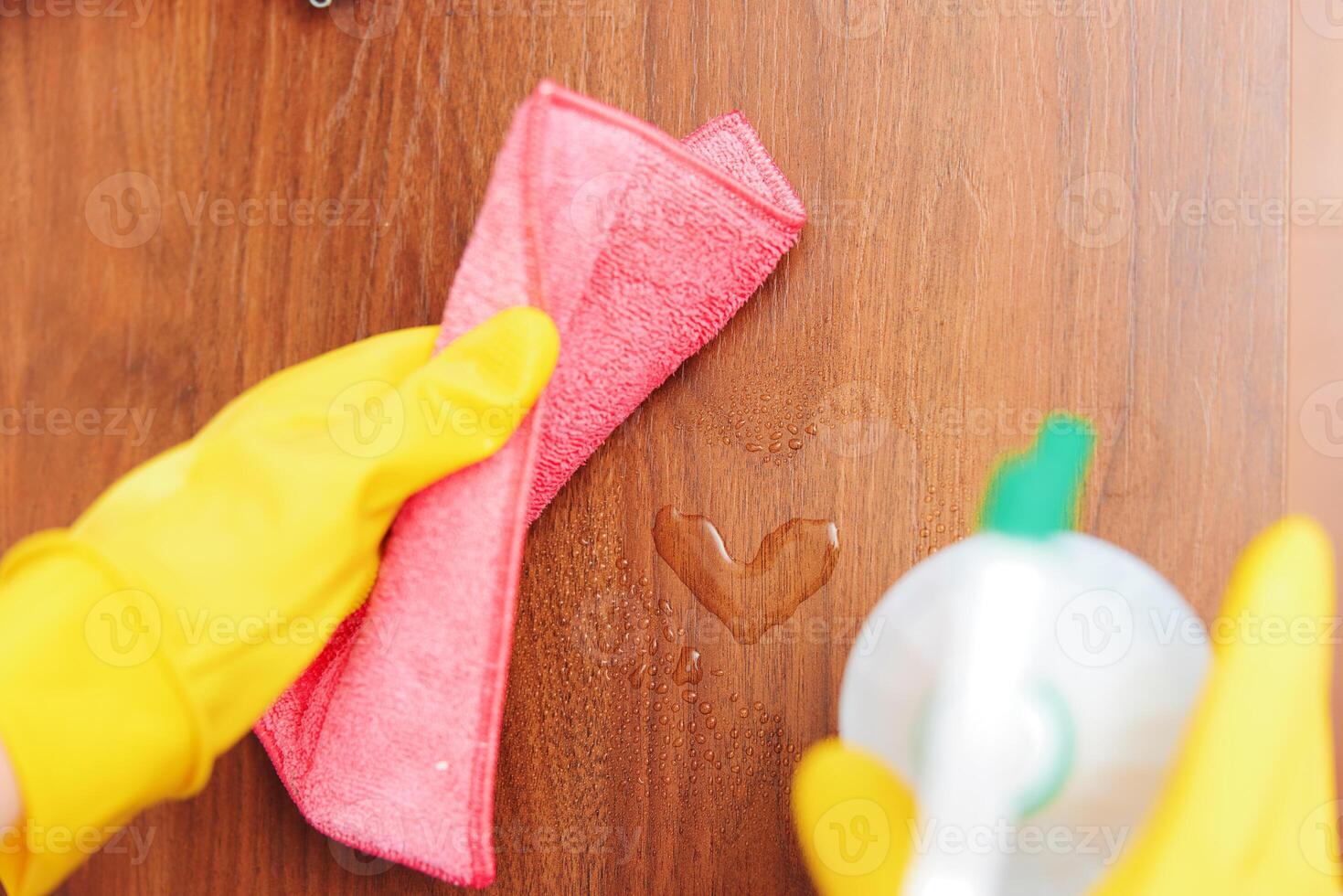 Woman in yellow gloves cleaning wooden surface with pink rag and green cleaning solution bottle photo