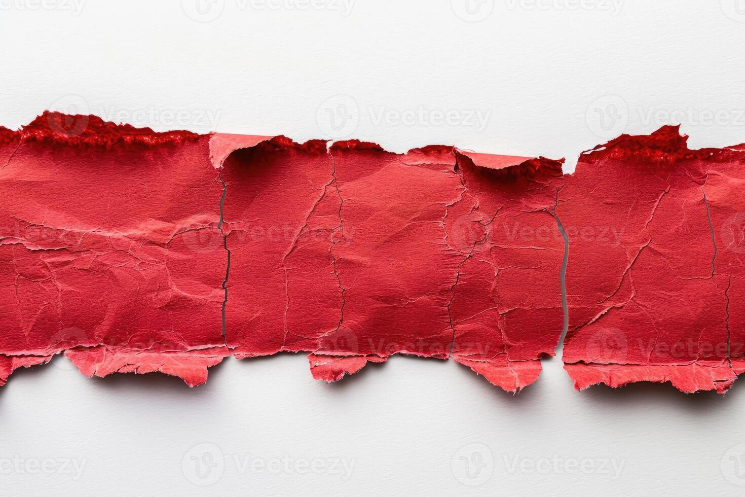 A torn piece of red paper rests on a white surface photo