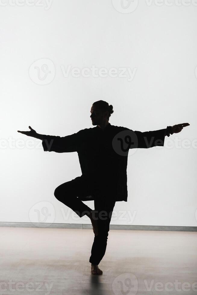 Silhouette of a person practicing qigong energy exercises on a light background photo