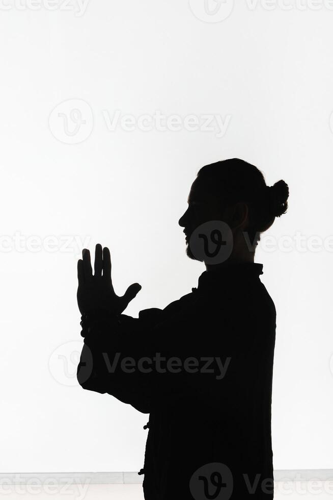 Silhouette of a person practicing qigong energy exercises on a light background photo