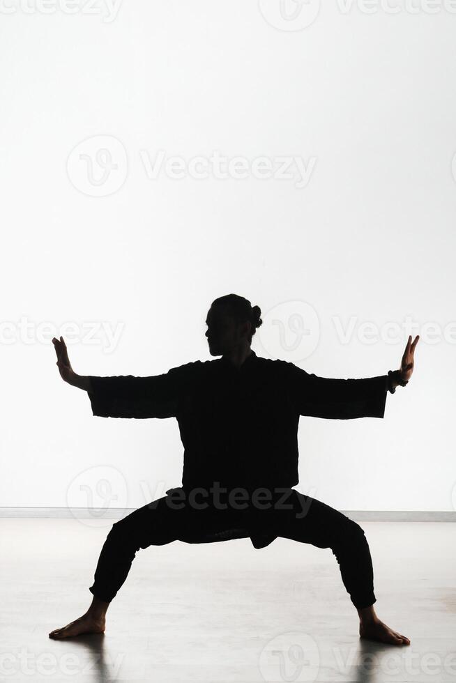 Silhouette of a person practicing qigong energy exercises on a light background photo