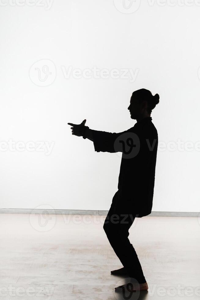 Silhouette of a person practicing qigong energy exercises on a light background photo
