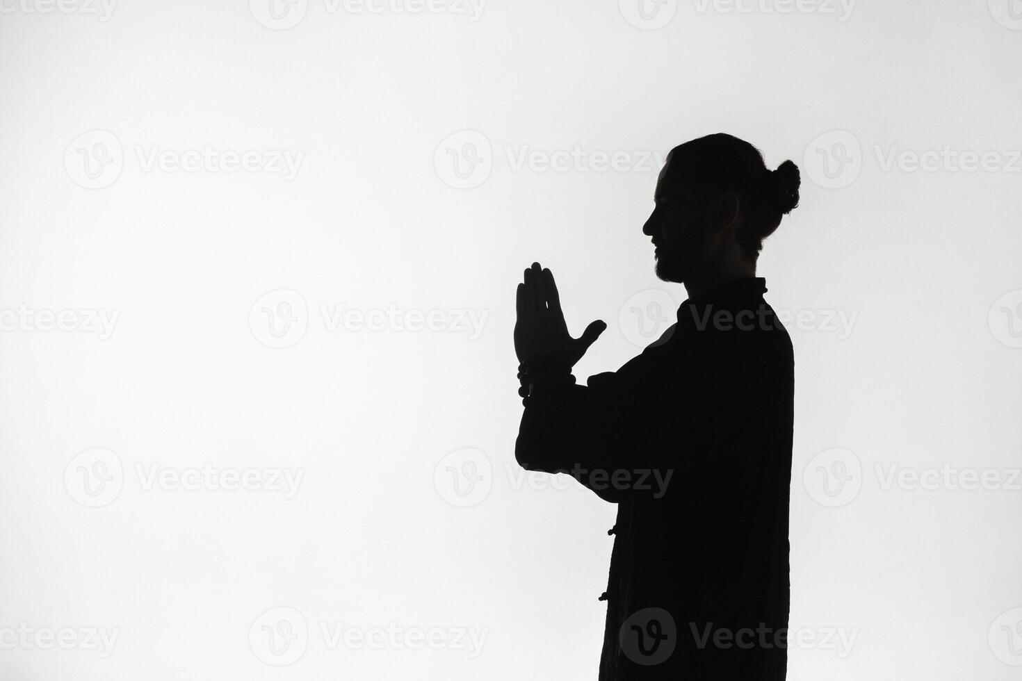 Silhouette of a person practicing qigong energy exercises on a light background photo