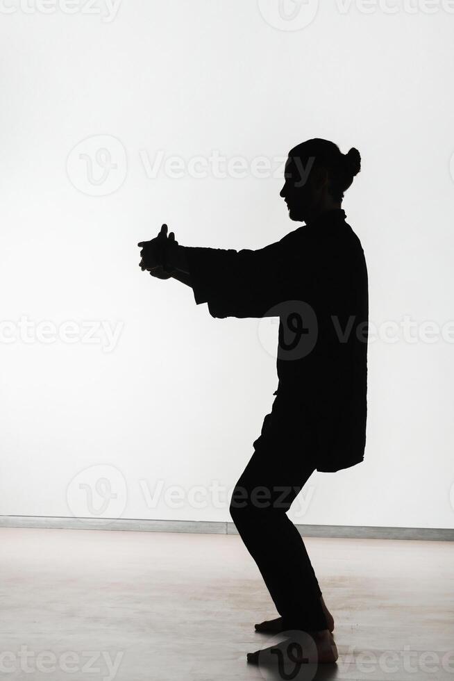 Silhouette of a person practicing qigong energy exercises on a light background photo