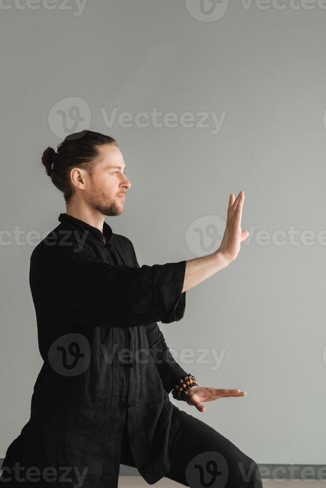 A man in black kimano practicing qigong energy exercises indoors photo