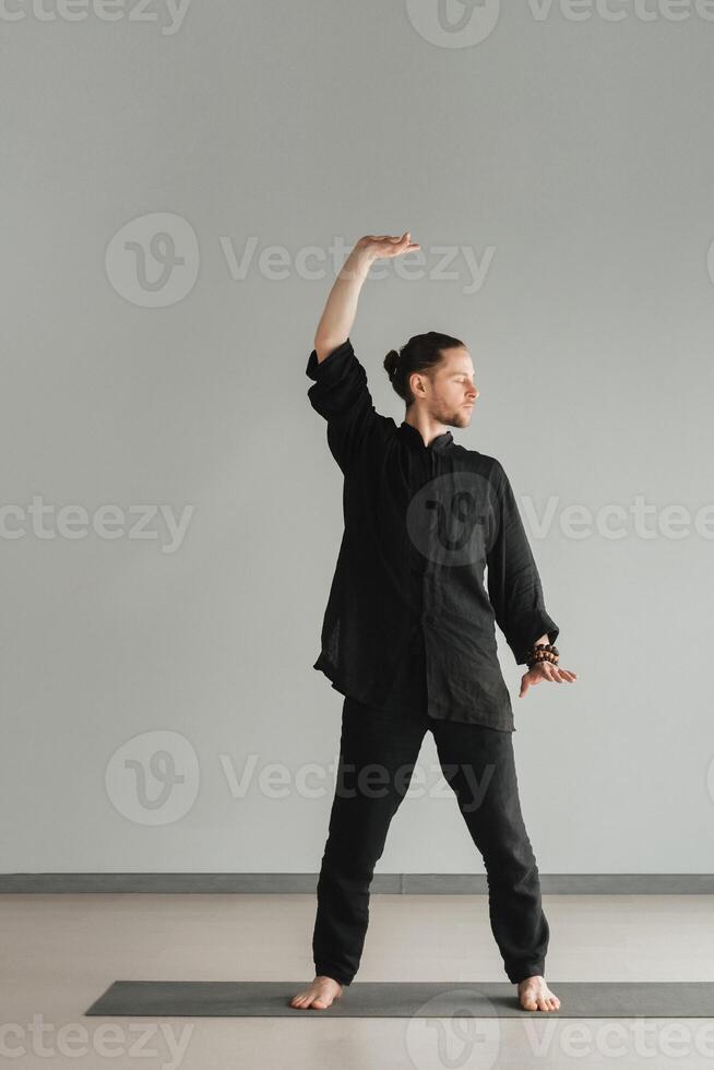 A man in black kimano practicing qigong energy exercises indoors photo