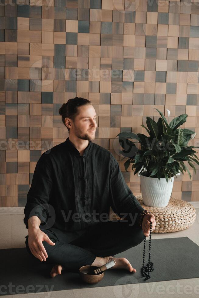 Portrait of a young man in a black kimano sitting in a lotus position on a gym mat in the interior photo