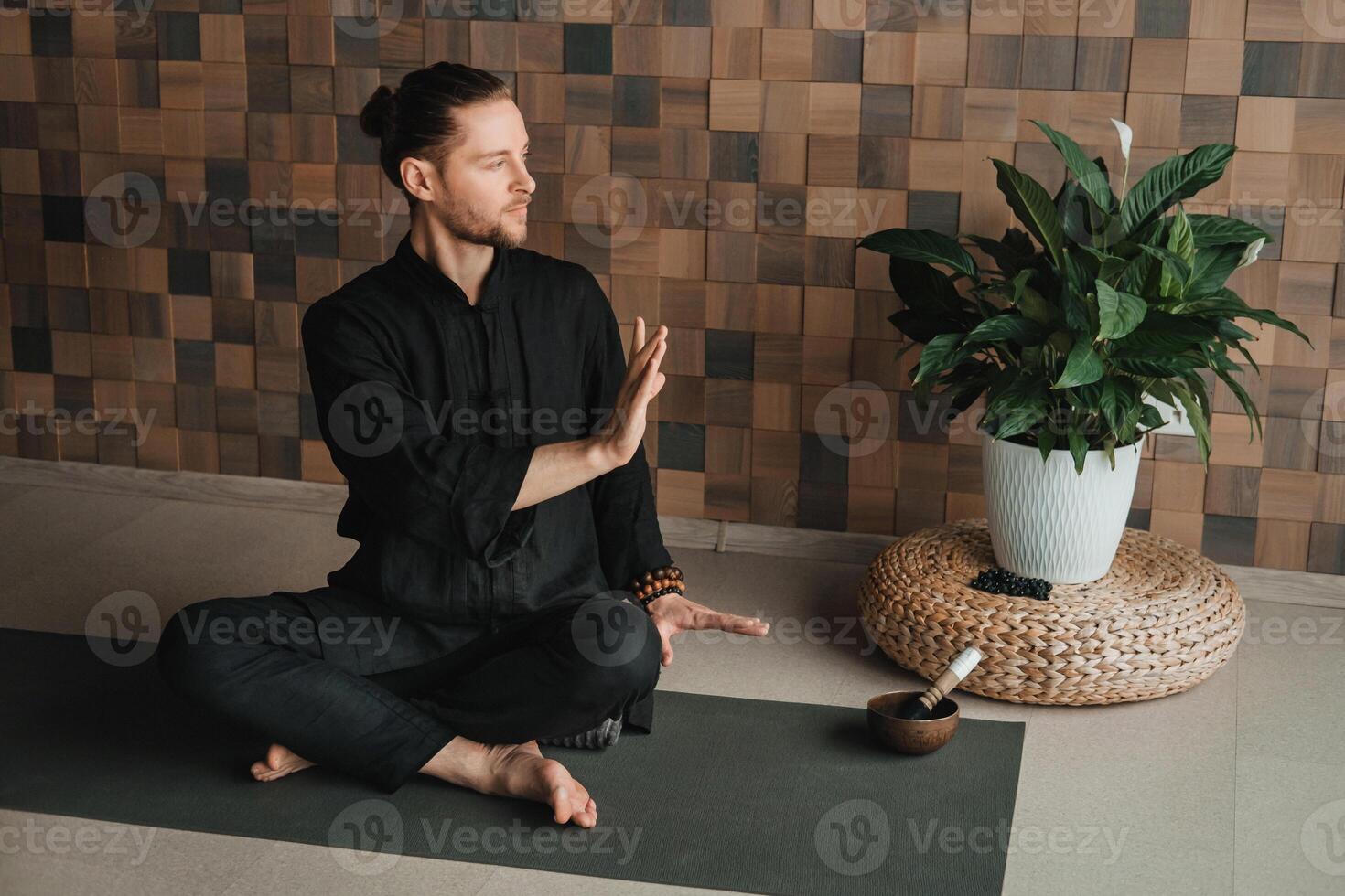 Portrait of a young man in a black kimano sitting in a lotus position on a gym mat in the interior photo