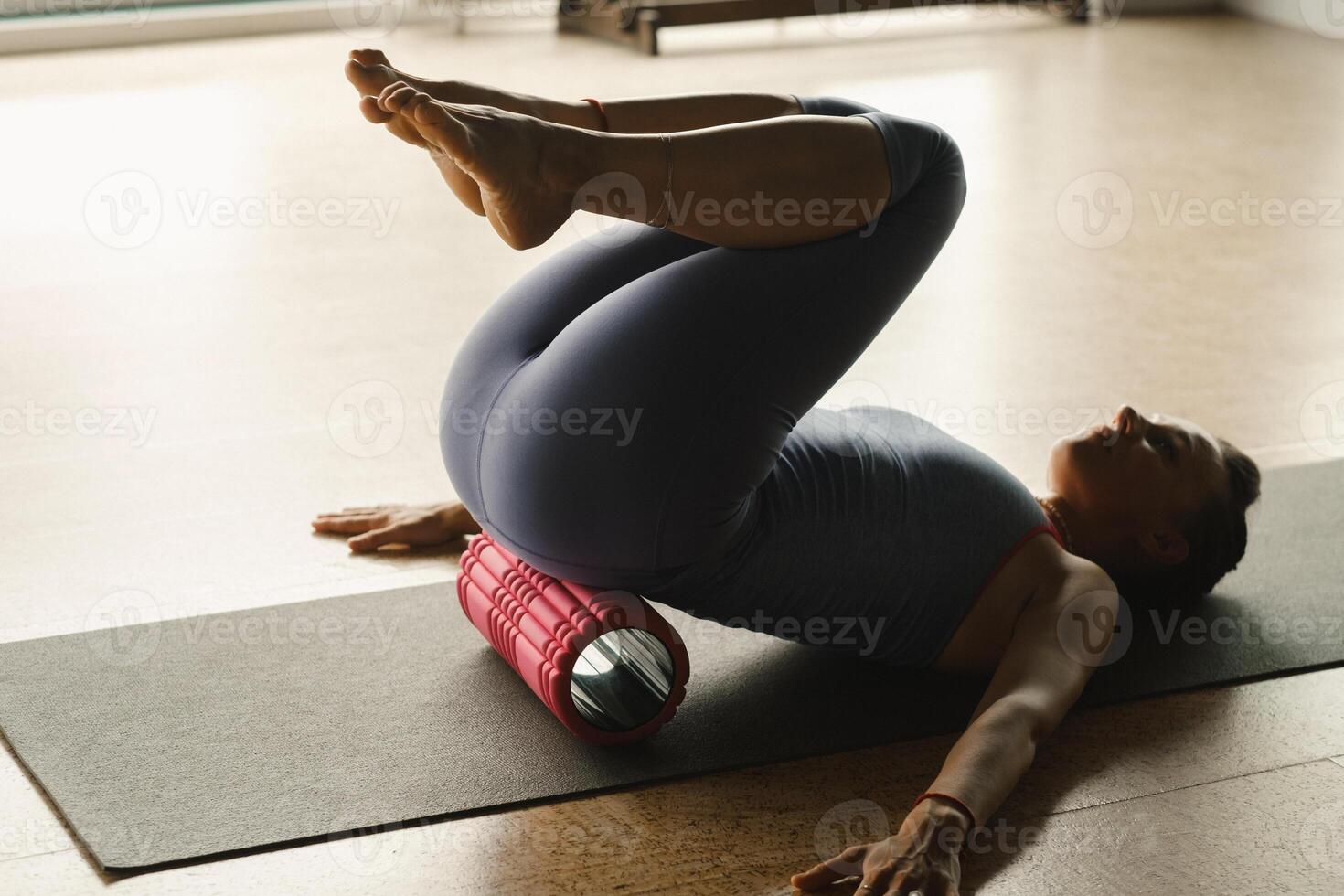Slender girl doing yoga with a big massage roller on the floor photo