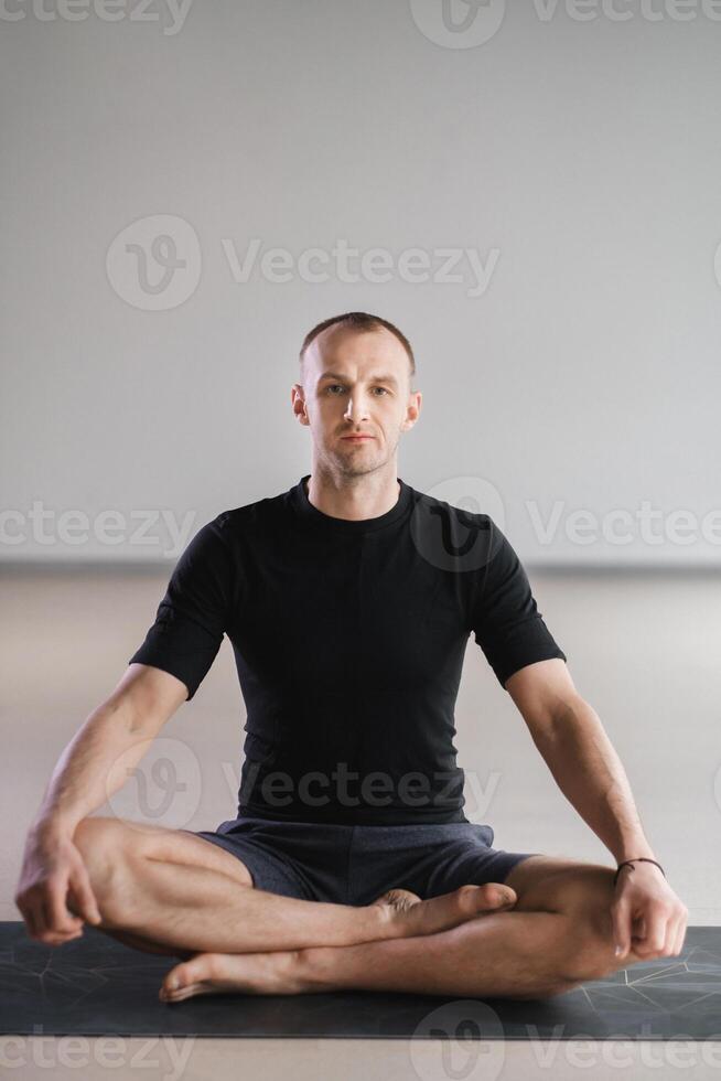 Portrait of an adult athletic man sitting in the lotus position in the gym on the mat photo