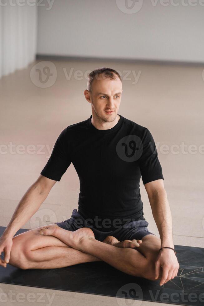 Portrait of an adult athletic man sitting in the lotus position in the gym on the mat photo