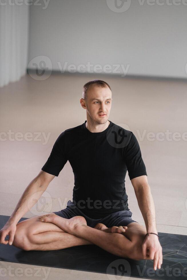 Portrait of an adult athletic man sitting in the lotus position in the gym on the mat photo