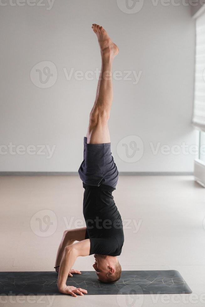 A man performs a yoga pose with support on his head in the gym. Yogi in a headstand photo