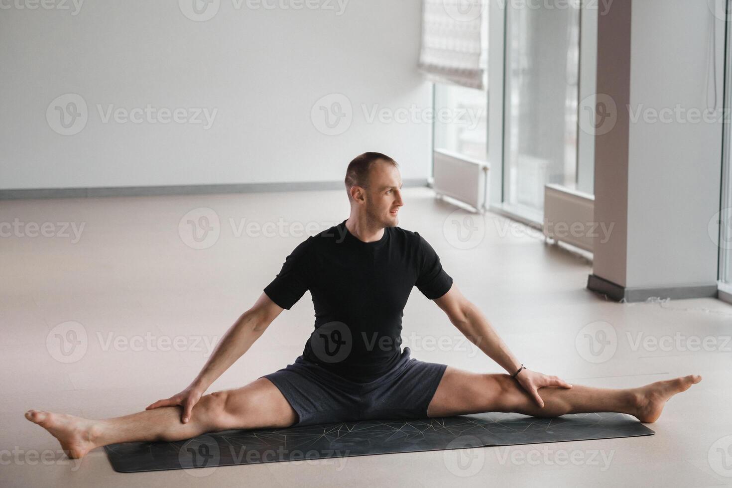 An athletically built man does yoga in the gym on a mat photo