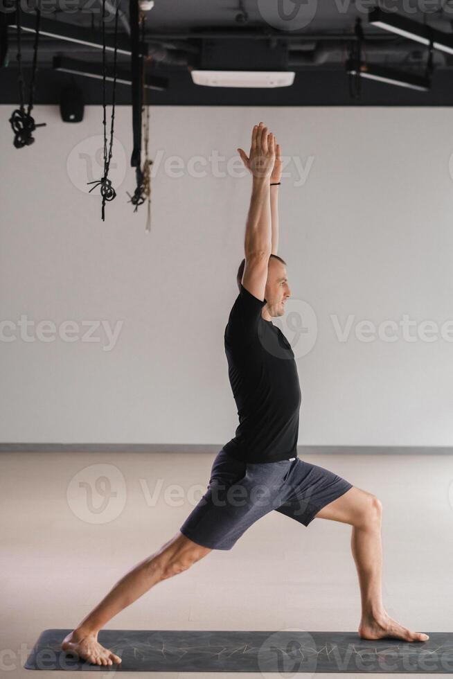 An athletically built man does yoga in the gym on a mat photo