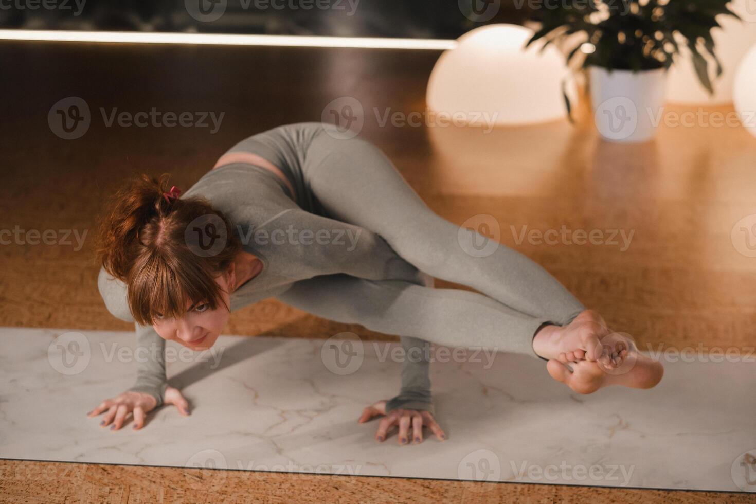 A girl in a gray sports uniform does yoga on a mat in the gym photo