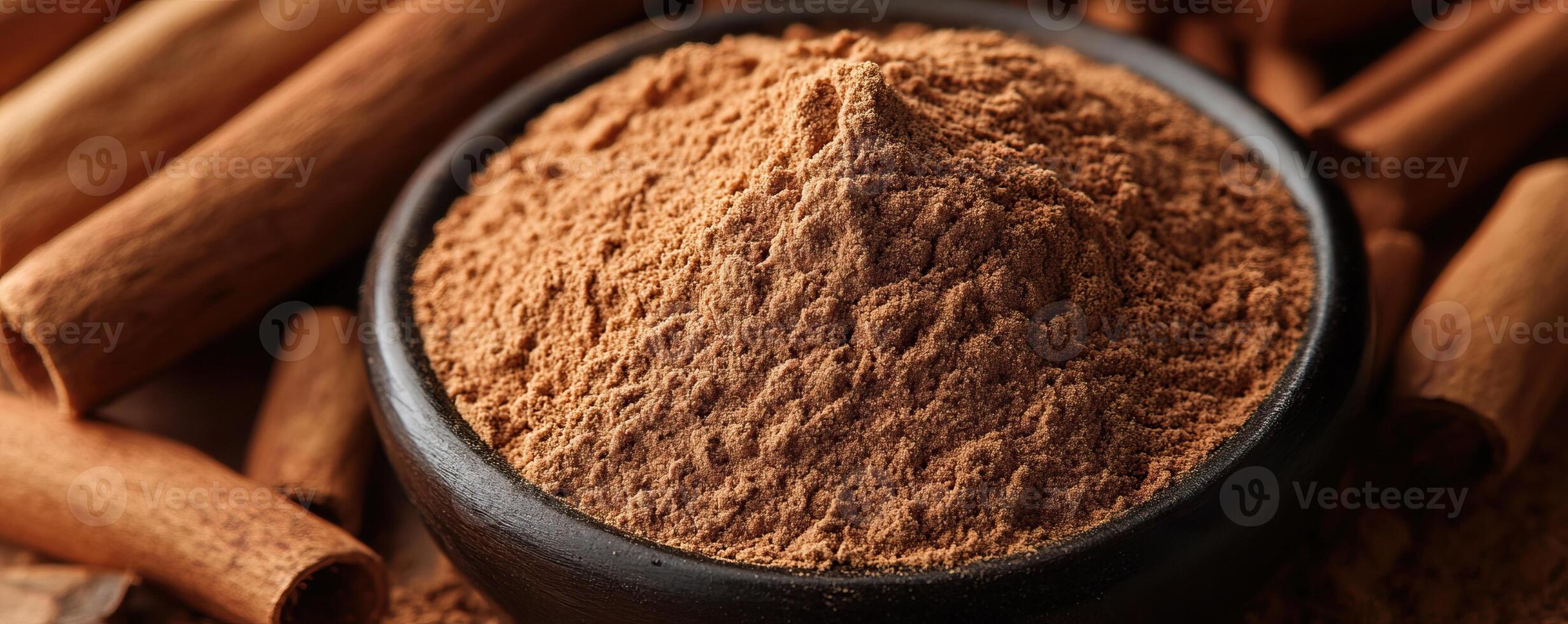 Cinnamon powder in a black bowl with whole cinnamon sticks on a dark background. photo