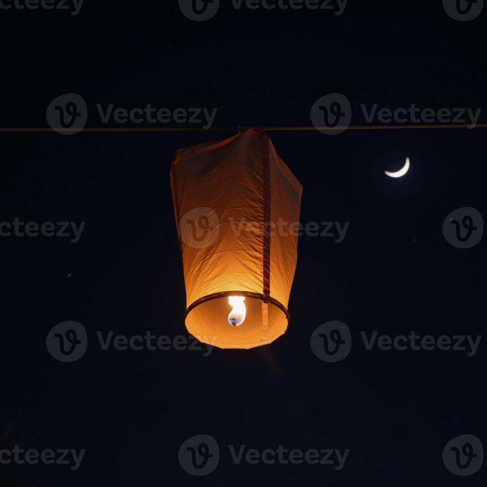 Lantern floats in night sky before crescent moon photo