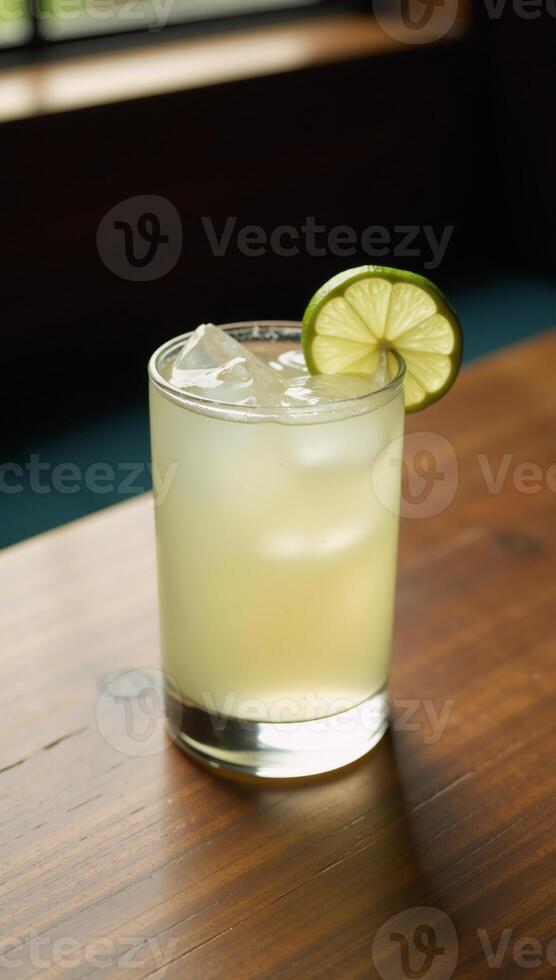 Clear glass filled with a refreshing margarita drink and garnished with lime slice serves invitingly on a rustic wood table photo