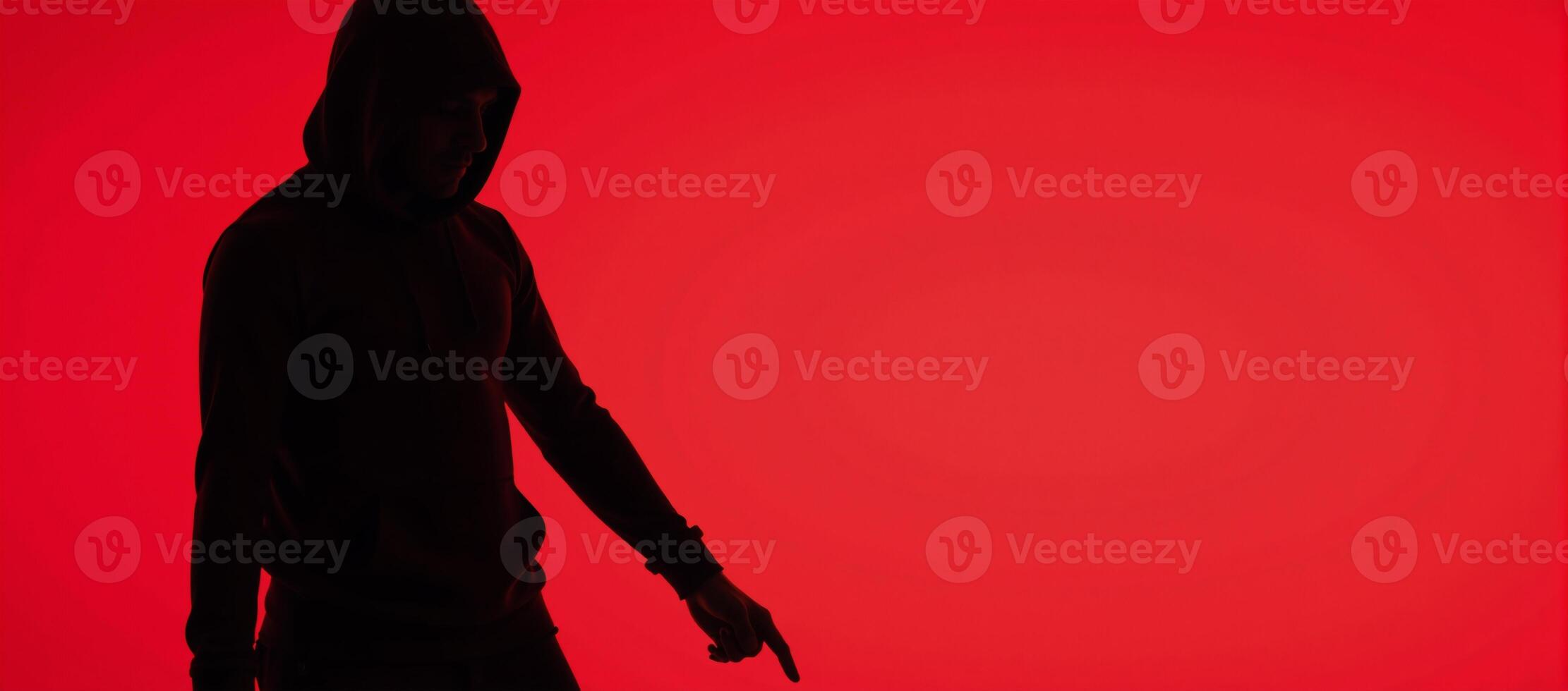 Man in hood with no visible face silhouetted against red background photo