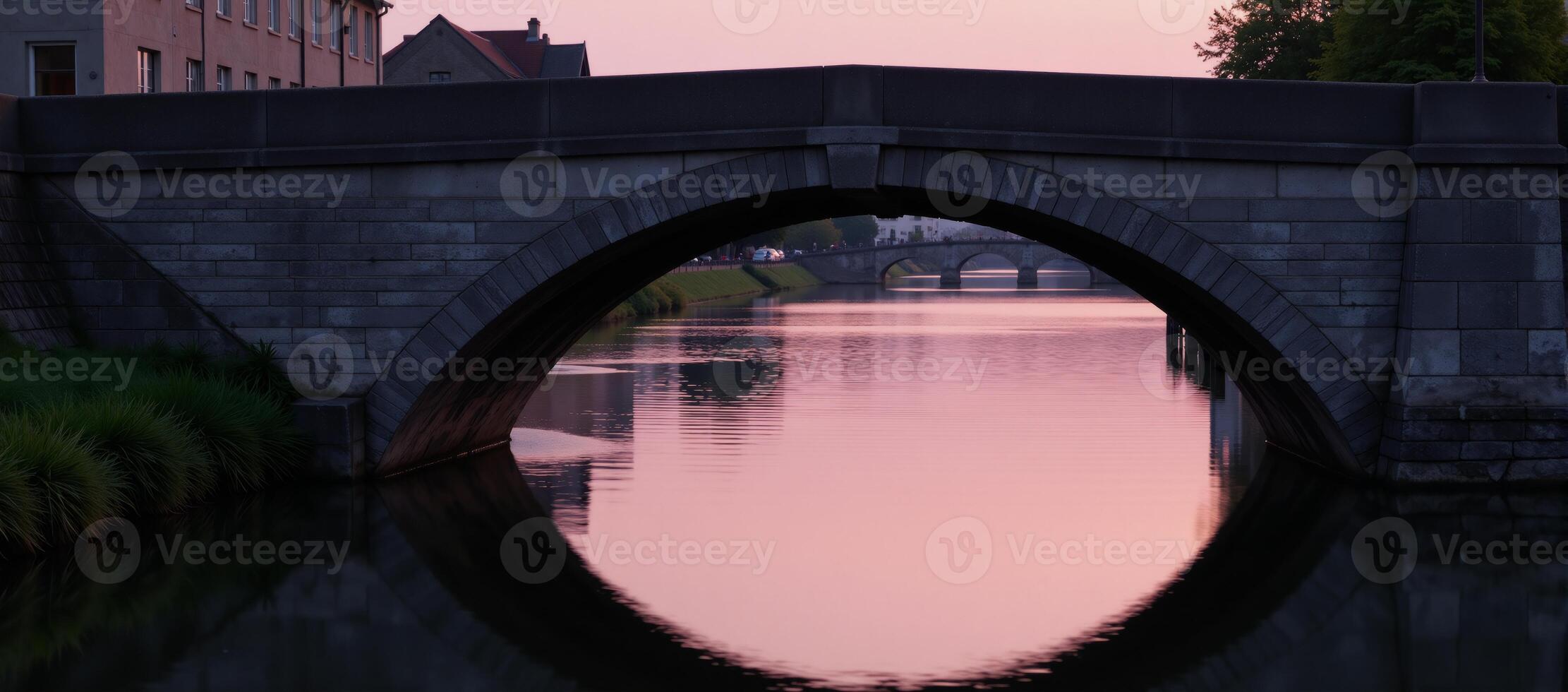 Stone bridge illuminated by soft pink light reflected on tranquil waters during twilight photo