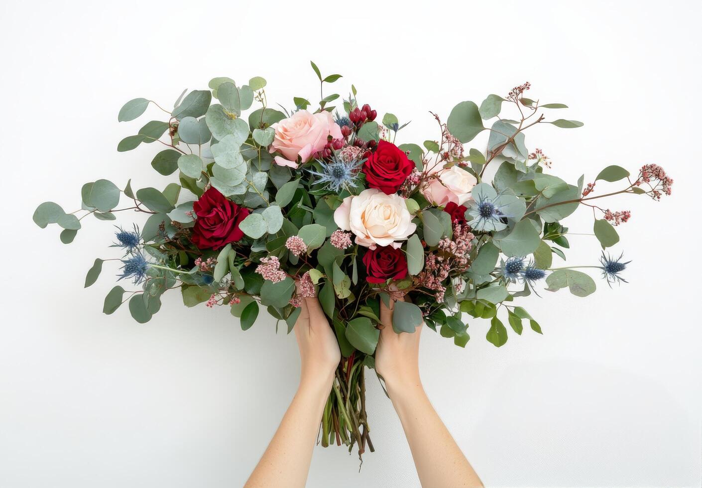 Two hands hold a pink and red rose arrangement with greenery against a neutral background photo