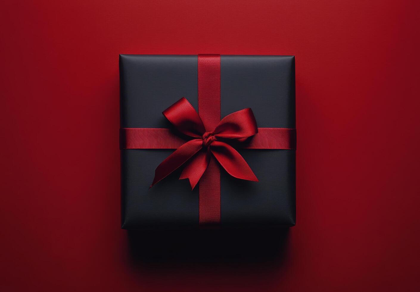 A beautifully wrapped black gift box with a red ribbon on a vibrant red backdrop photo