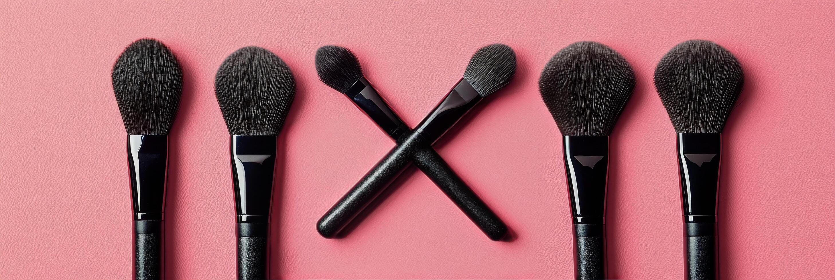 A set of makeup brushes in varying shapes on a pink background photo