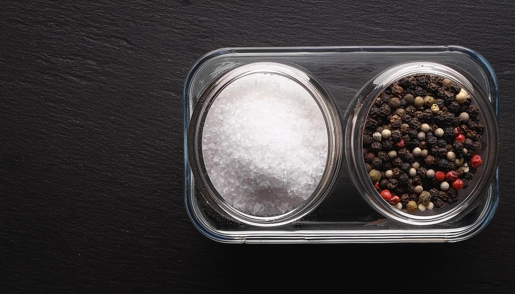 Sea salt and pepper in a container, on a black background photo