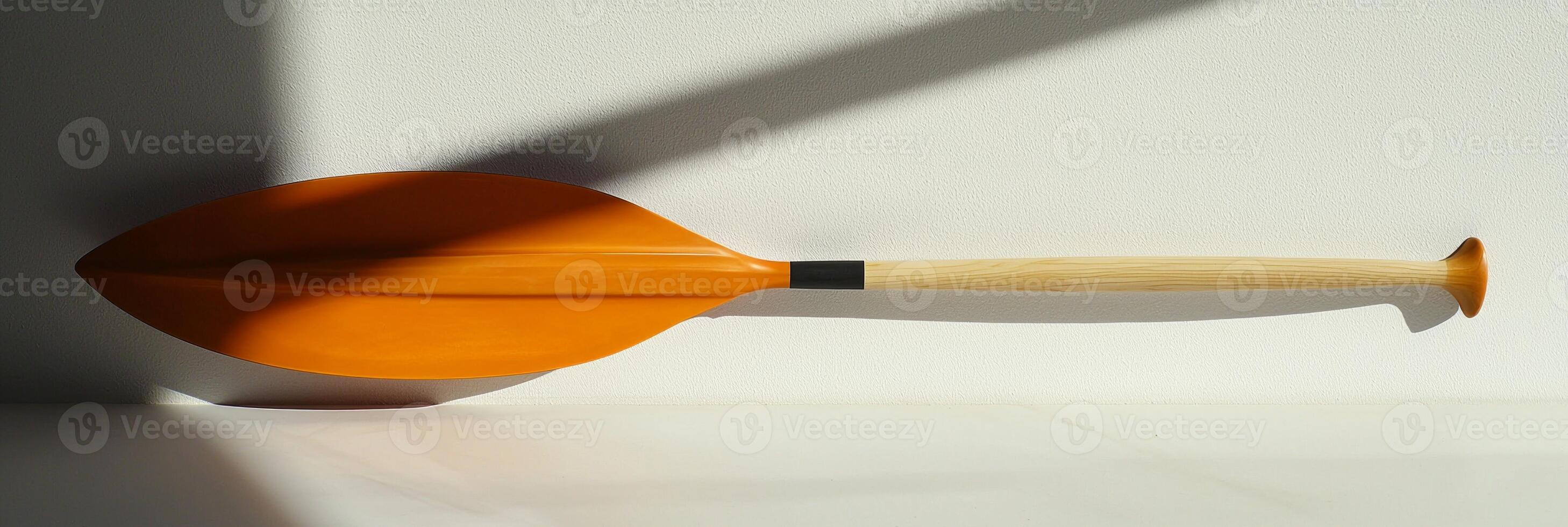 canoe paddle rests on a white background highlighting its vibrant blade shape and comfortable handle grip. Soft shadows create a striking visual effect in bright lighting. photo