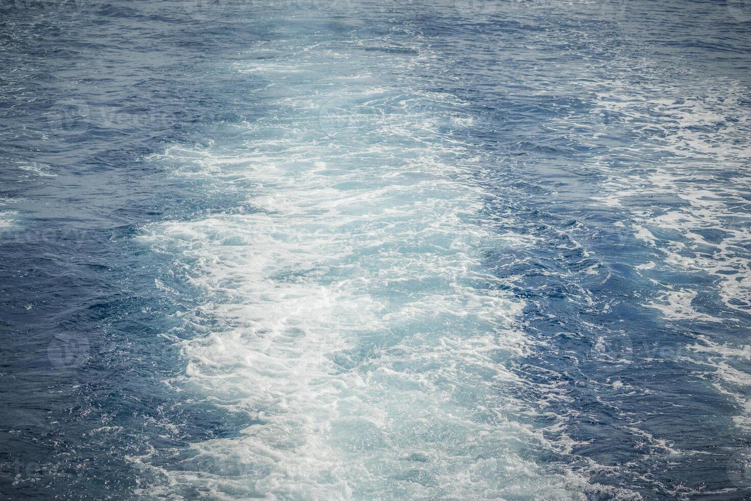 Wake of a ship creating frothy, white trails on the blue ocean surface. photo