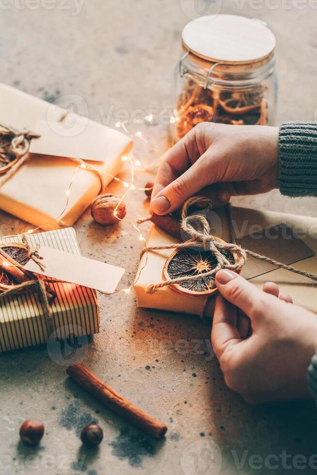 Female hands packaging gift in craft paper, decorated by natural decor. Zero waste christmas concept photo
