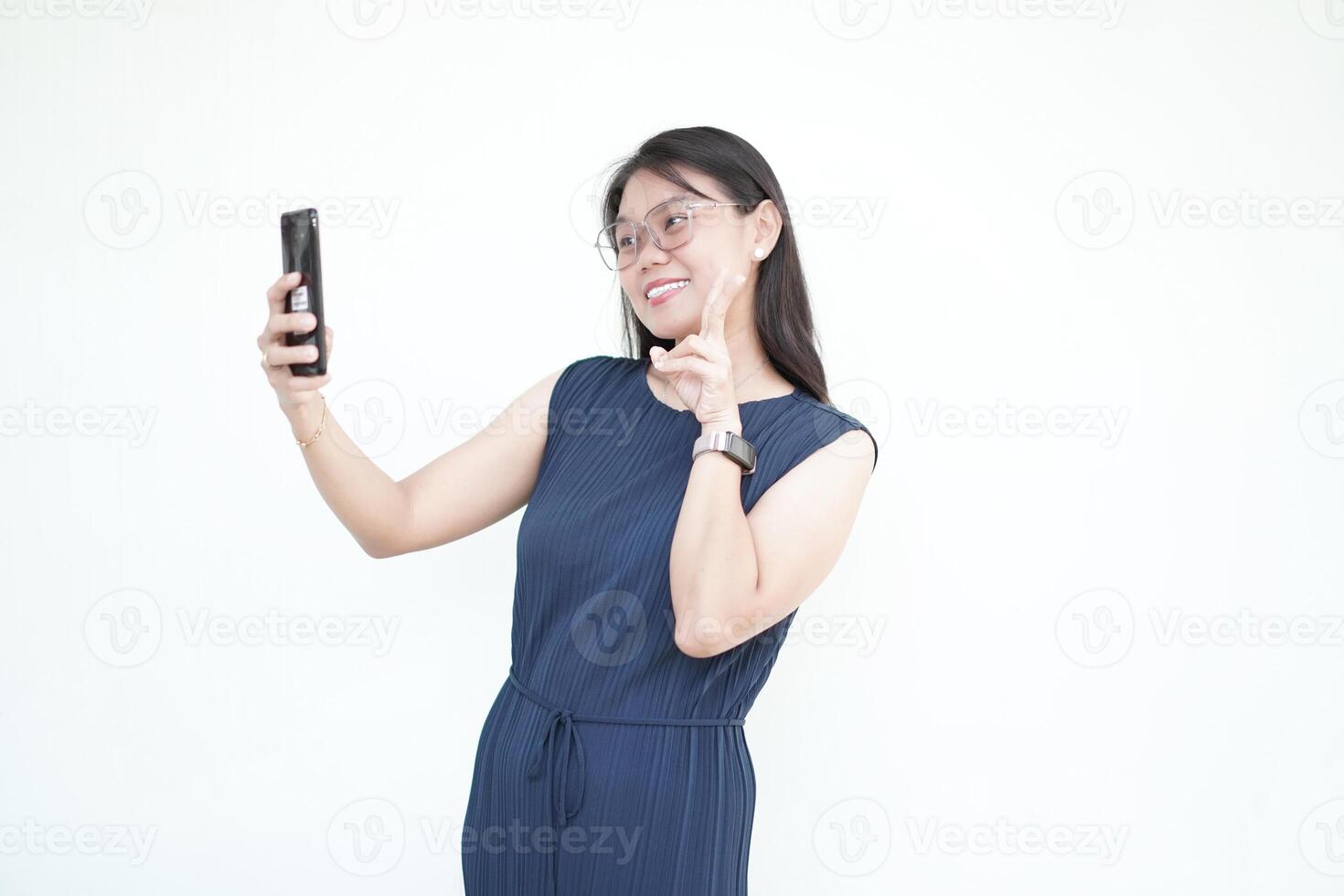 Beautiful Asian woman holds a smartphone, capturing a cheerful selfie against a white background photo