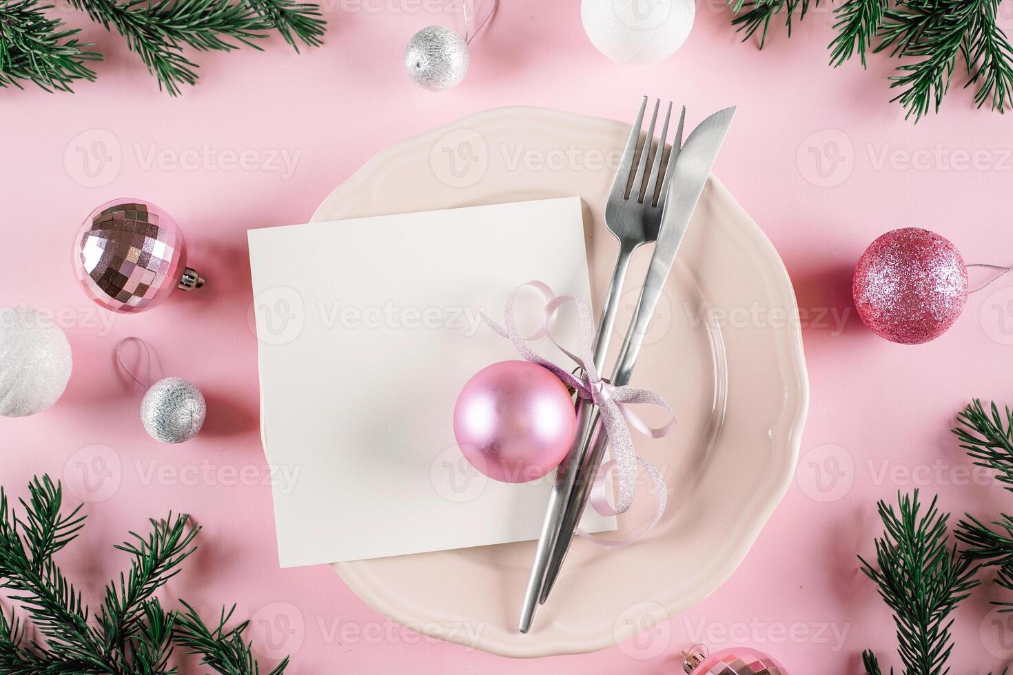 Christmas table setting on pink background. White plate and silver utensils. Festive holiday decoration photo