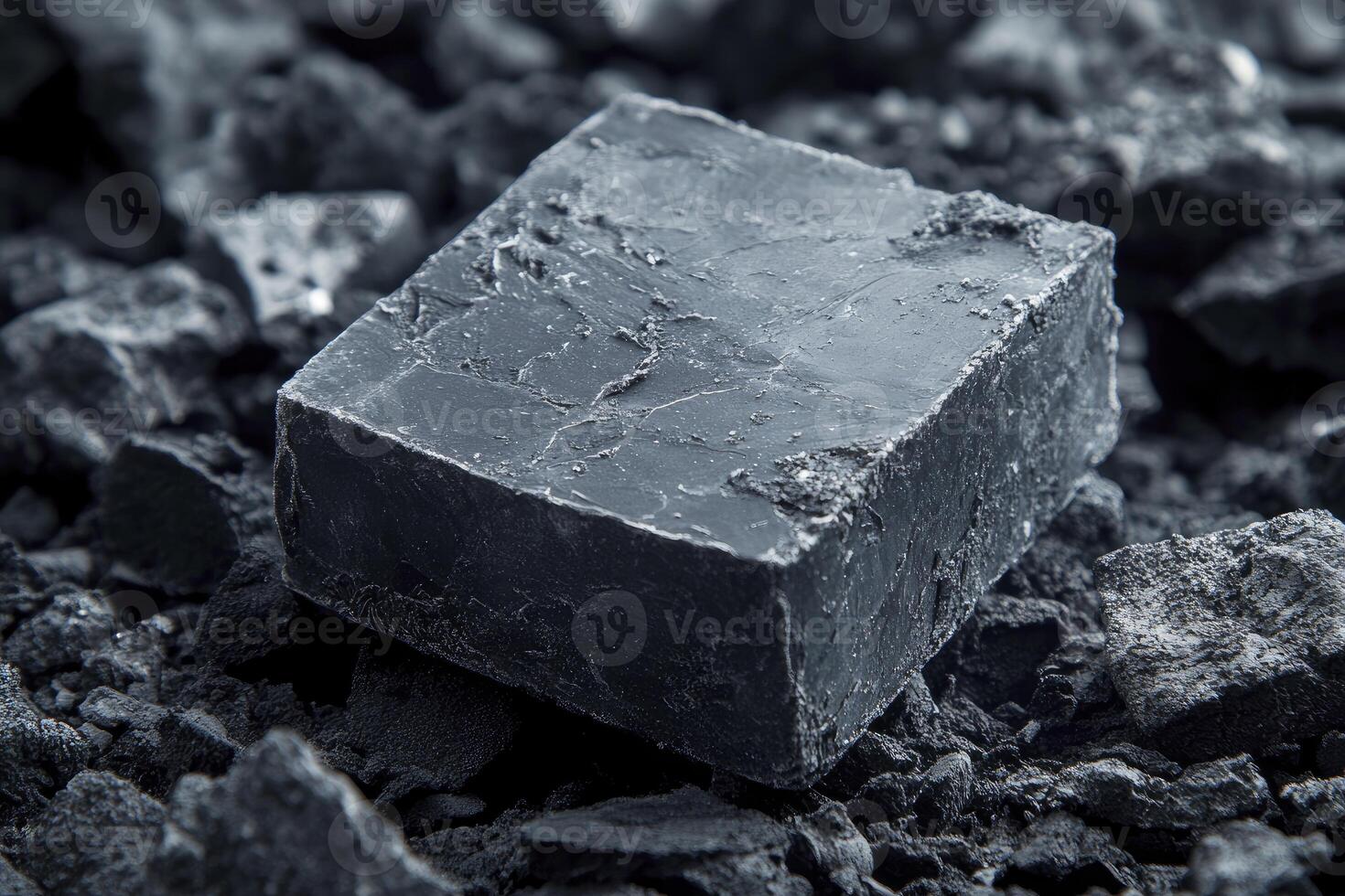 A black cube of coal sitting on top of a pile of coal photo