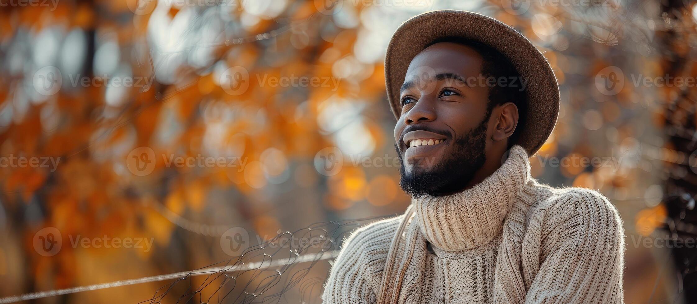 A man in a sweater and hat smiles in the fall photo
