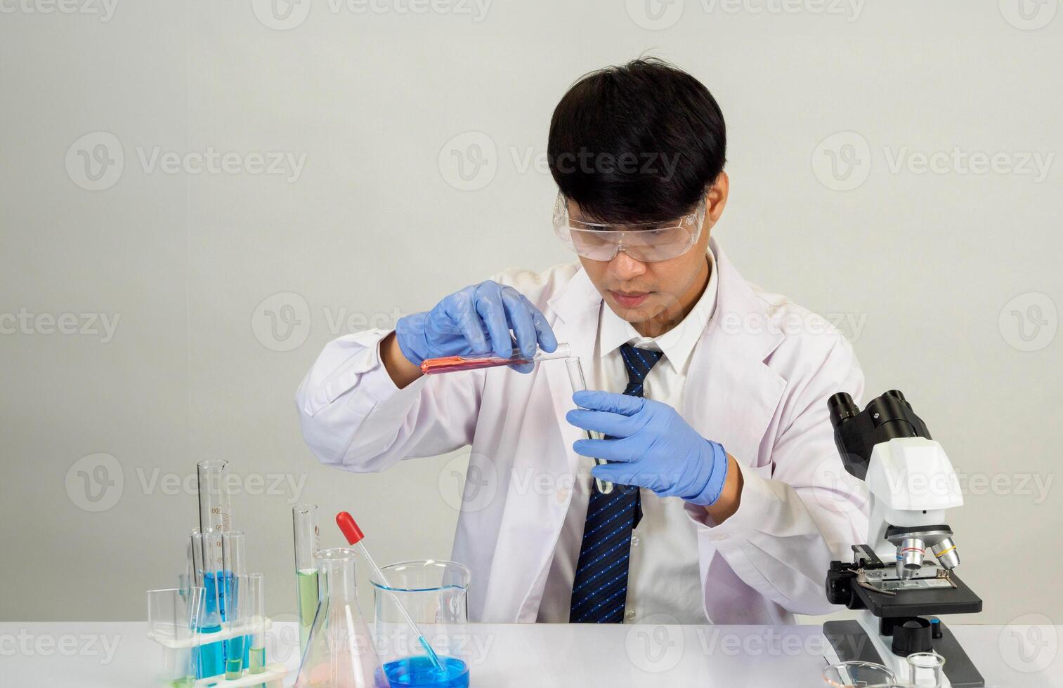 Man asian student education learning scientist wearing doctor gown in lab looking hand at chemist. caused by mixing reagents in scientific research laboratories with test tubes and microscope on table photo