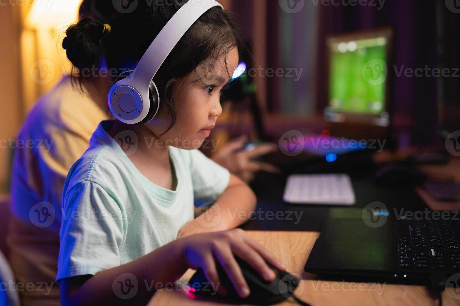 Asian young girl is playing a game with a computer mouse. She is wearing headphones and she is focused on the game photo
