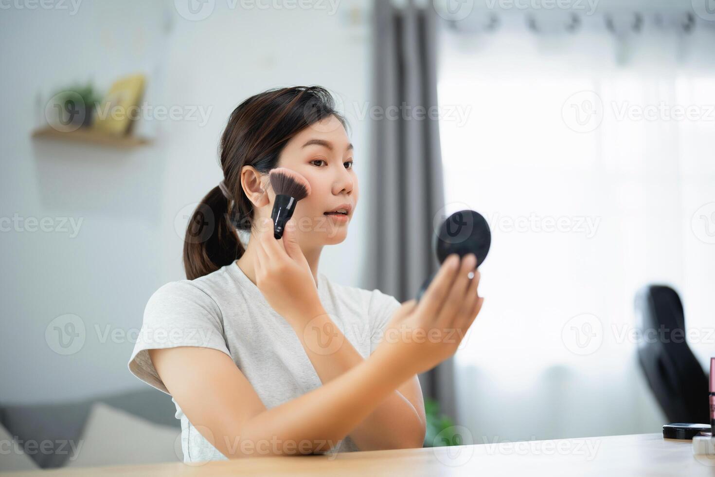 Asian woman is applying makeup in front of a mirror. She is using a brush to apply the makeup photo