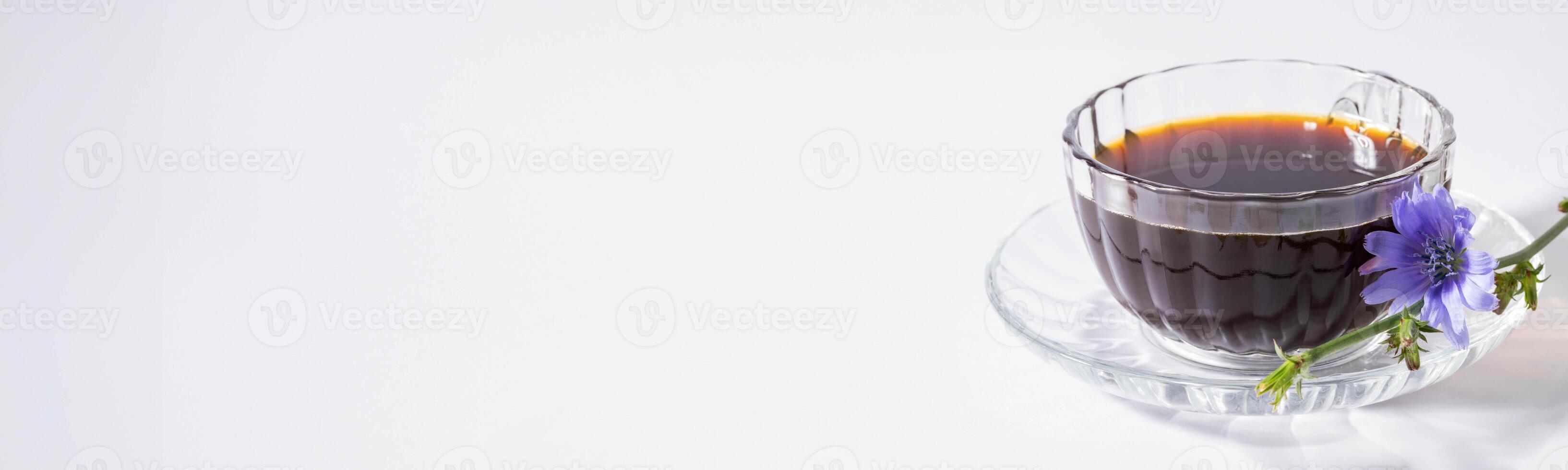 Figured glass transparent cup of chicory tea on saucer, its flower on white. Banner. Copy space. photo
